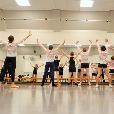 Children practicing dance moves in a studio with mirrors.