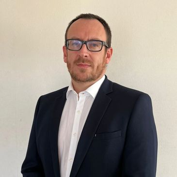 Man in glasses wearing a black suit and white shirt.