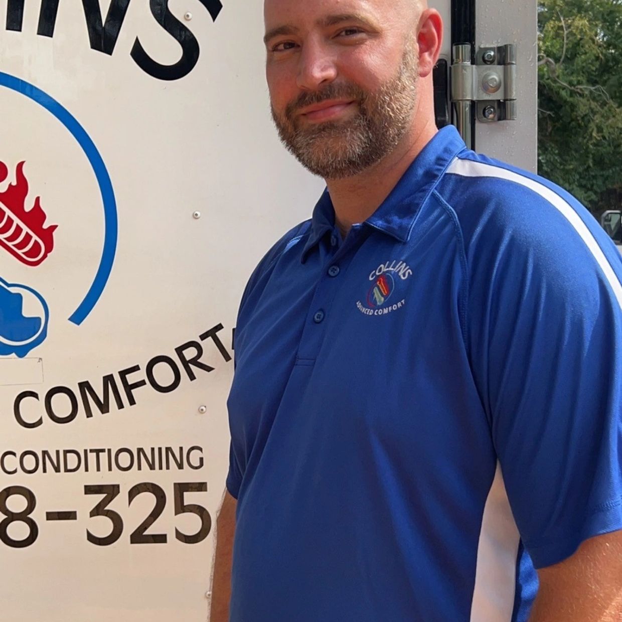 Man in blue Collins Advanced Comfort shirt standing beside branded vehicle.