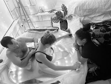 Pregnant woman labouring in birth pool with partner and midwife supporting her