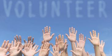 Many hands raised to the sky with  VOLUNTEER written in the clouds