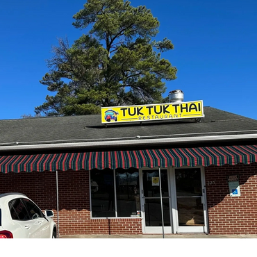 Exterior view of Tuk Tuk Thai restaurant with a striped awning and clear blue sky.