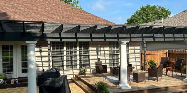 Outdoor patio with pergola, seating, and grill under sunny sky.