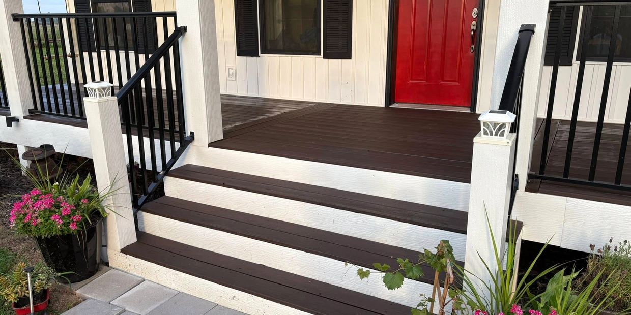 Front porch with brown steps, black railings, red door, and potted flowers.