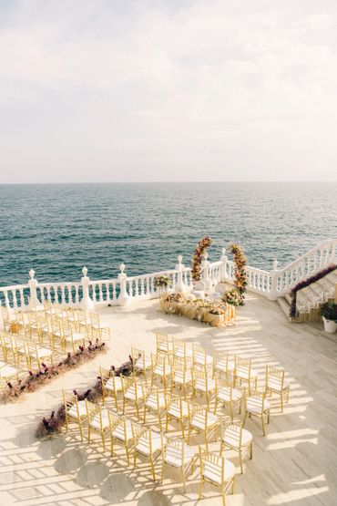 Elegant seaside wedding setup with golden chairs and floral decorations. Antalya Wedding Planner