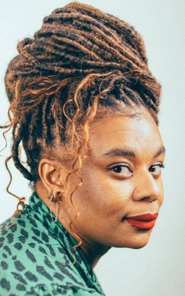 Woman with stylish dreadlocks and red lipstick wearing a green patterned top.