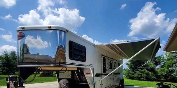 A shiny white camper trailer with an extended awning under a blue sky.