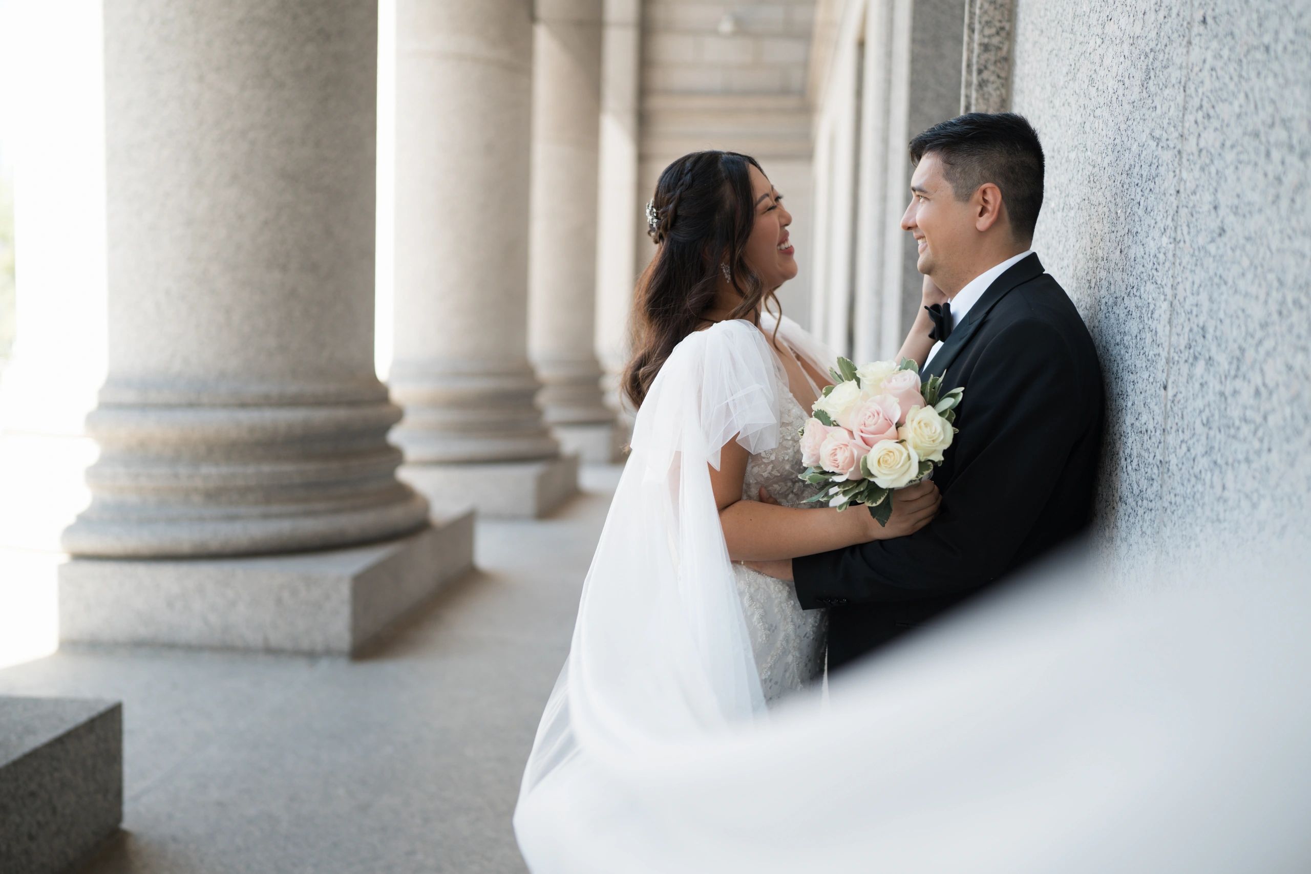 Happy bride and groom sharing a joyful moment by stone columns.