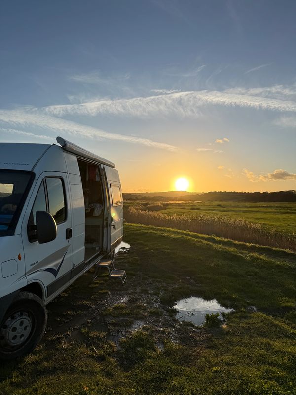 A van parked in a grassy field during a golden sunset.