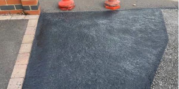 Freshly paved black asphalt patch on a pavement corner.