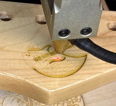 A laser engraver etching a guitar design onto wood.