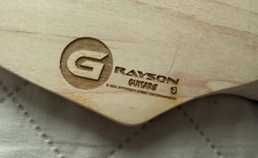 Close-up of a wood engraving on a guitar labeled Grayson Guitars.
