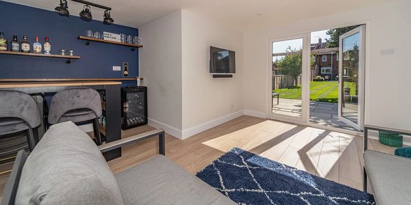 Modern living room with bar area and garden view through glass doors.