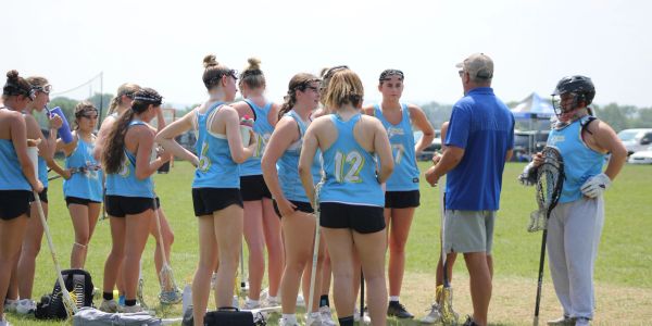 Girls' lacrosse team receiving coaching on field.