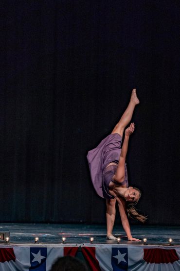 Dancer performing a high kick on a stage with patriotic decorations.