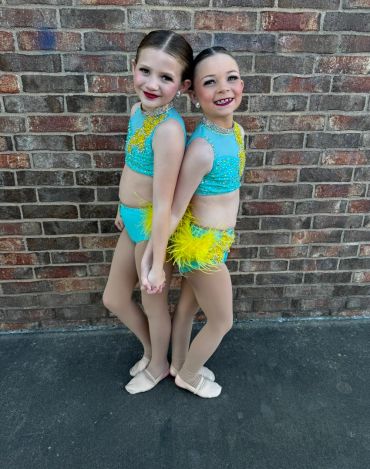 Two young girls in blue and yellow dance costumes pose together.