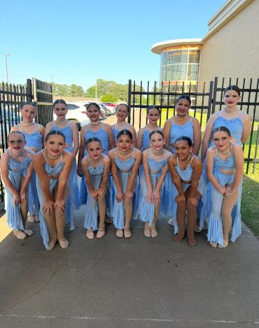 Group of young dancers posing outdoors in light blue costumes.