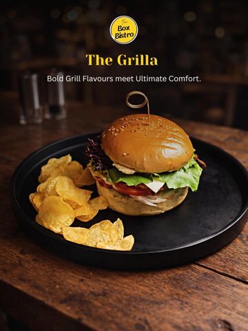 A grilled chicken burger with chips on a black plate at Box Bistro.