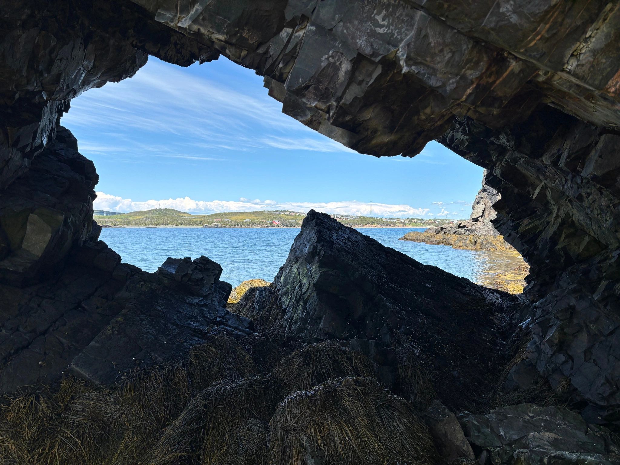 View of Arnold’s Cove framed by a rocky coastal cave along the Warpath/Otter Rub Trail