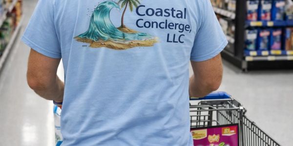 Person wearing a Coastal Concierge LLC shirt pushing a shopping cart in a store.