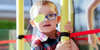 A young boy with glasses and a star-shaped eye patch plays on a playground.