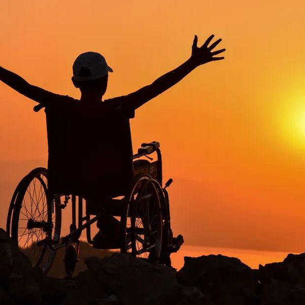 A disabled person sitting on a wheel chair and enjoying sunset