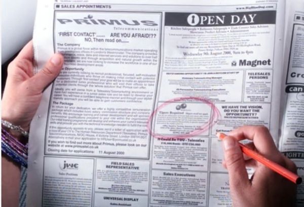 Hands marking a newspaper classified ads section with an orange pen.