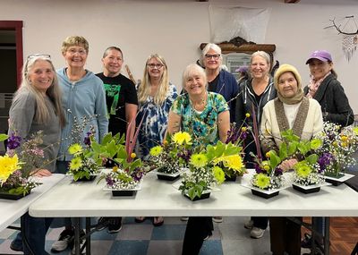 Group of women proudly displaying flower arrangements at a workshop.