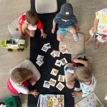 Children sitting in a circle playing a card game with cushions.
