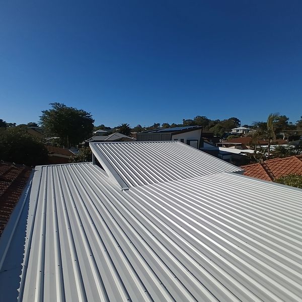 Clear blue sky over residential rooftops with metal and tiled roofs.
