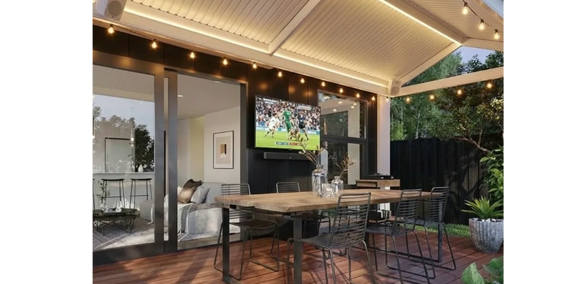 Modern outdoor dining area with string lights and a TV under a covered patio.