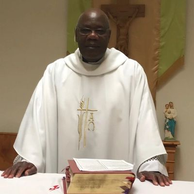 A priest standing behind a Bible on an altar, dressed in white vestments.
