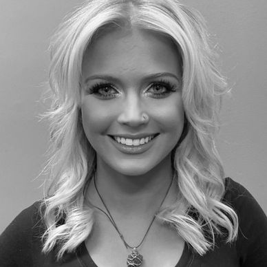 Smiling woman with wavy blonde hair and a pendant necklace.