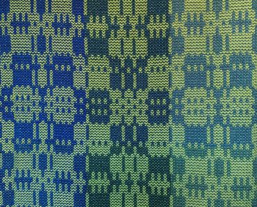 Woven fabric with repeating skull patterns in blue and green shades.