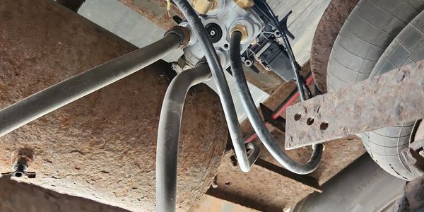 Rusty vehicle undercarriage with pipes, hoses, and a tire in view.