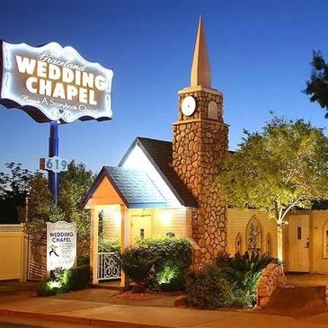 Illuminated small wedding chapel with stone clock tower at night.