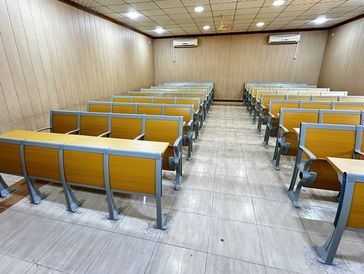 Empty classroom with yellow and gray desks arranged in rows.