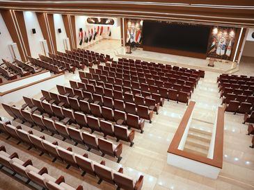Empty auditorium with rows of brown seats and flags on stage.