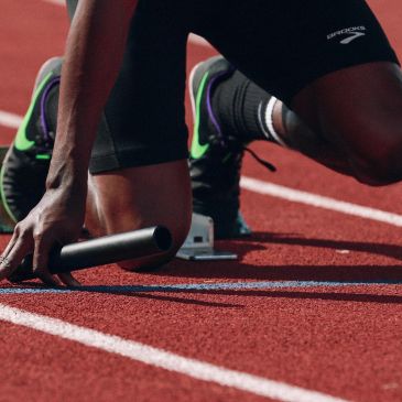 Athlete in starting position holding a baton on a running track.