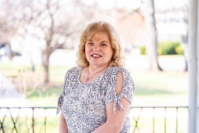 Smiling woman with blonde hair standing outdoors on a sunny day.