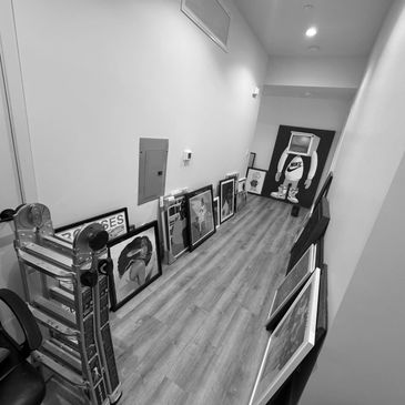 A black and white photo of art ready to be installed, lining a hallway with a folded ladder on the l