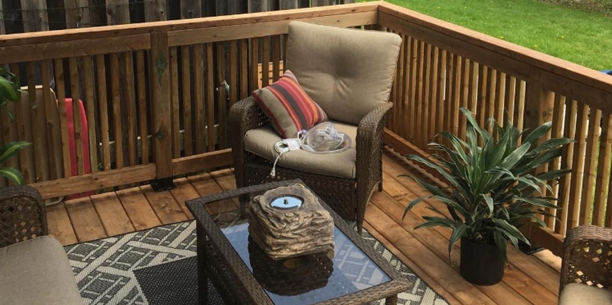Cozy outdoor deck with cushioned chairs, a glass coffee table, and a potted plant under a large umbrella.