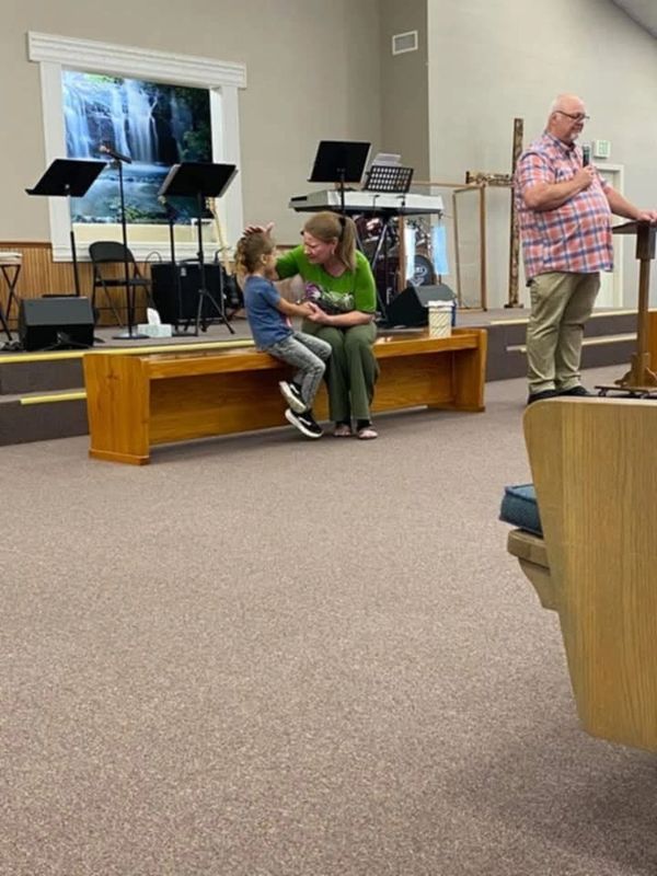 Woman talking with child in a church setting, man speaking at podium.
