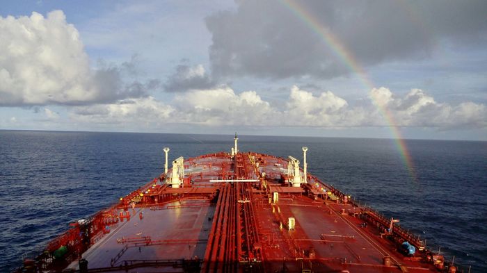 A ship sailing under a rainbow on a partly cloudy day.