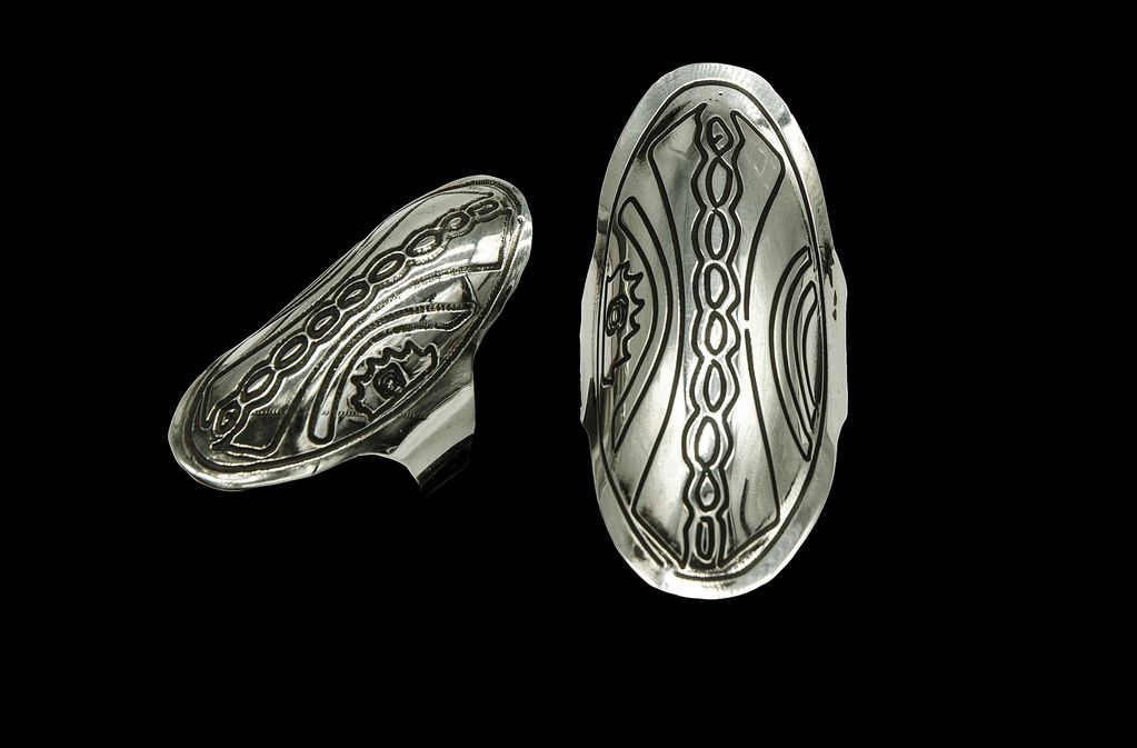 Two silver rings with intricate designs on black background.