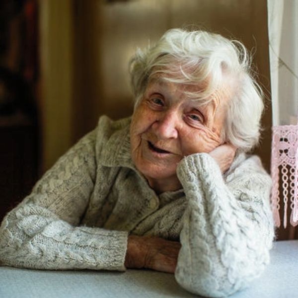 Elderly woman with a warm smile resting by a window.