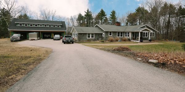 A countryside house with a large driveway and garage surrounded by trees.