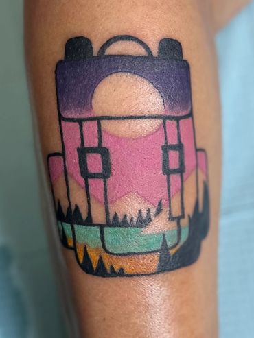 Full color tattoo of a backpack with mountain scenery.