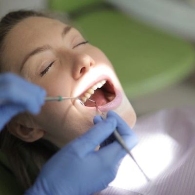 Patient receiving dental examination with mouth open and dentist's hands in blue gloves.