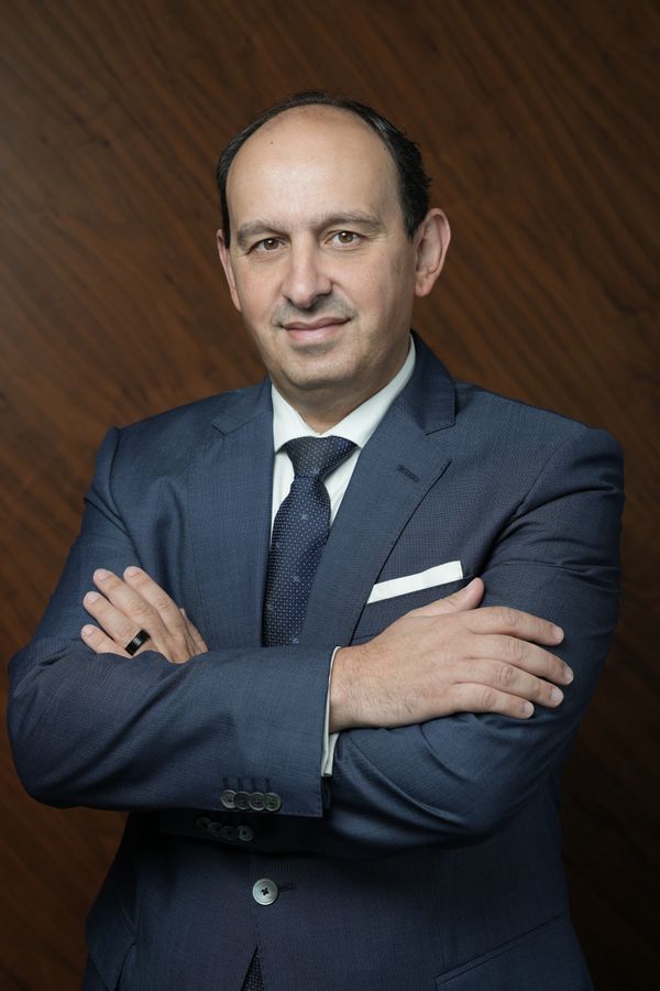 Confident man in a blue suit with arms crossed, smiling gently.